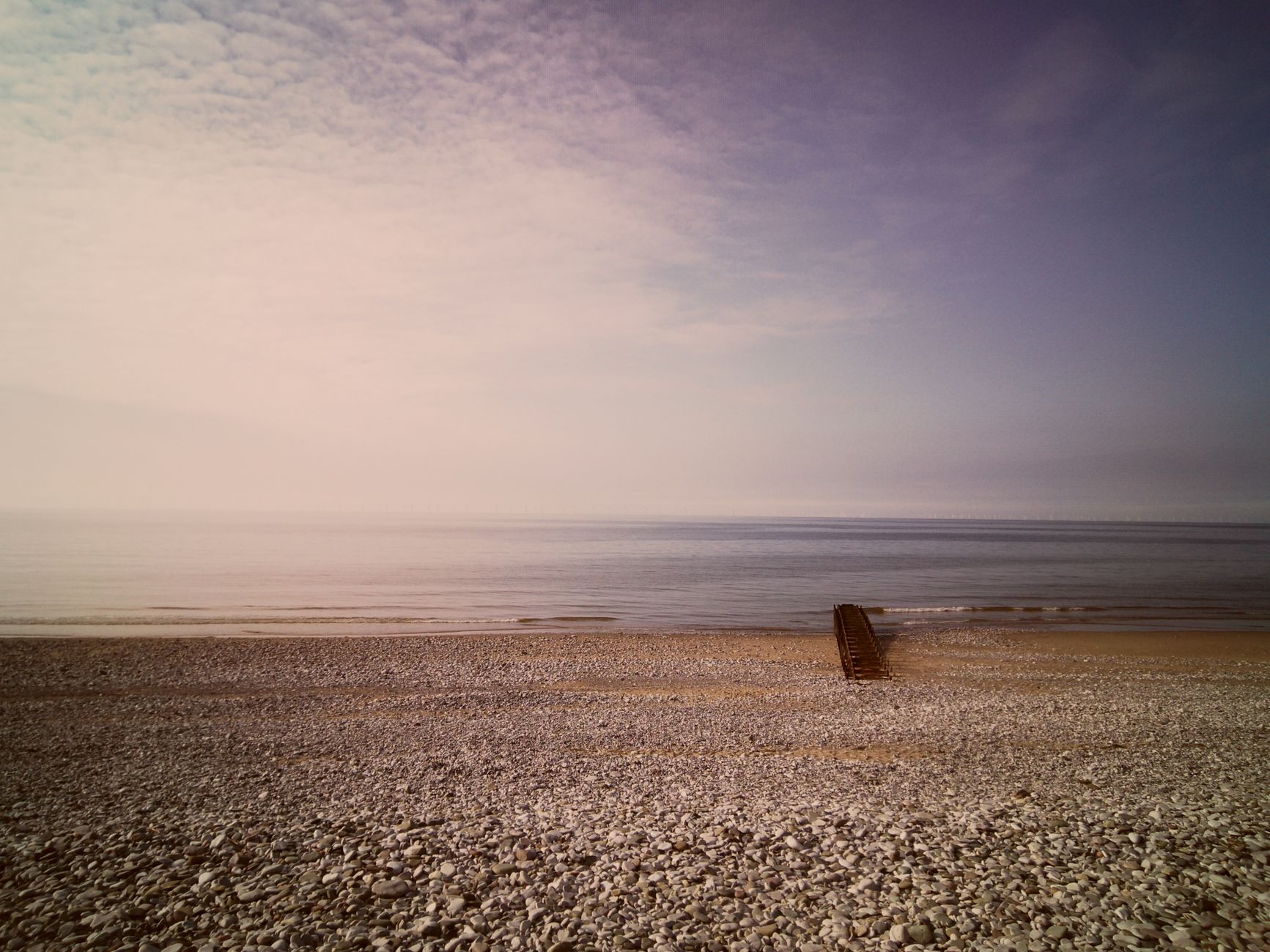 Stenstrand ved havet under en lys, diset himmel