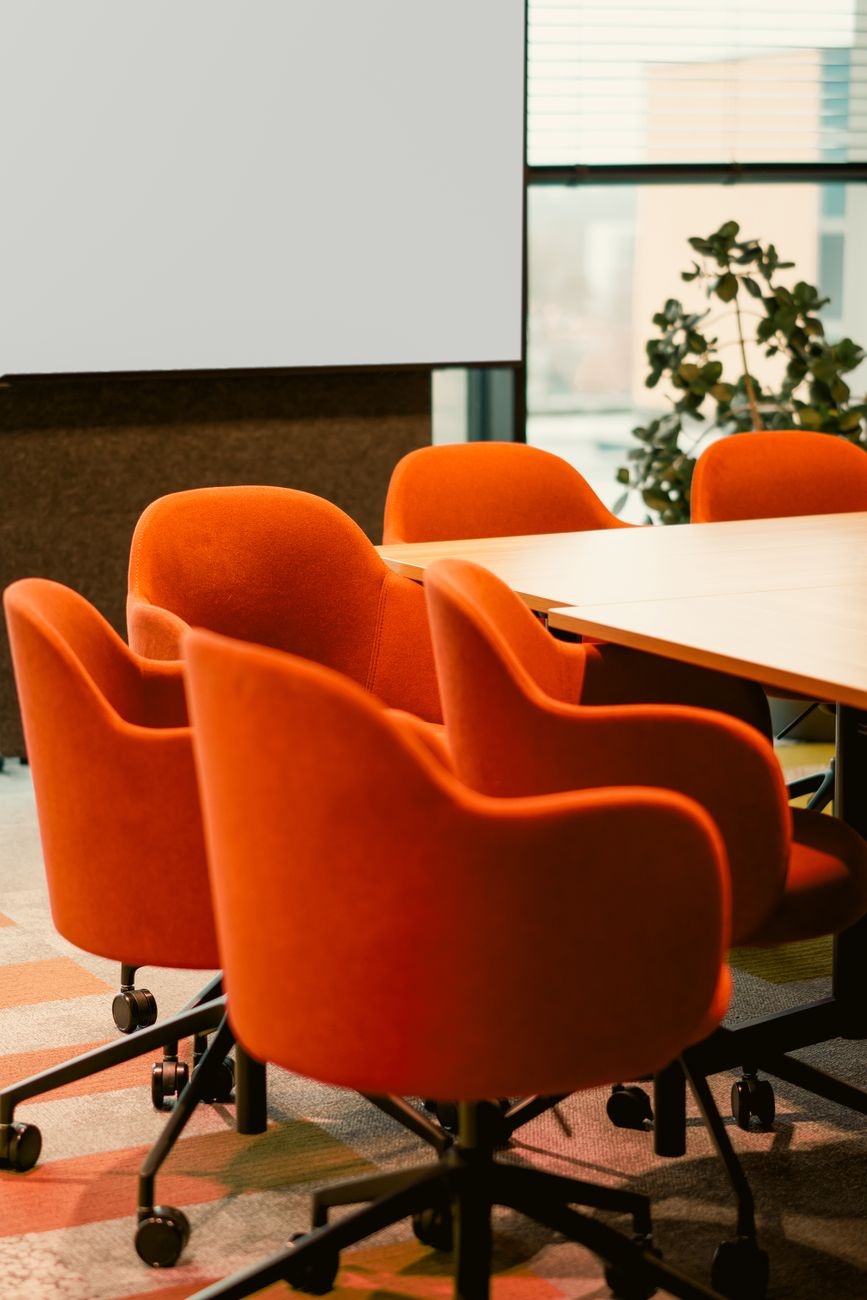 Orange stole omkring et mødebord i et lyst lokale
